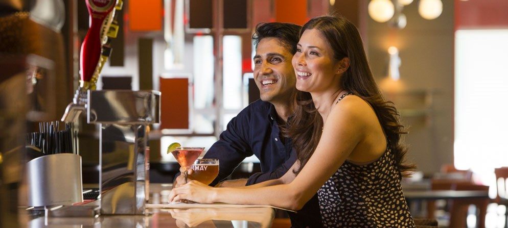 a man and woman sitting at a bar with a drink